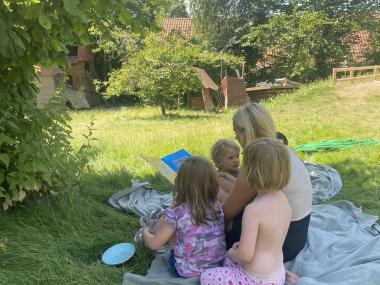 Børn læser bog på græsset, sammen med en voksen